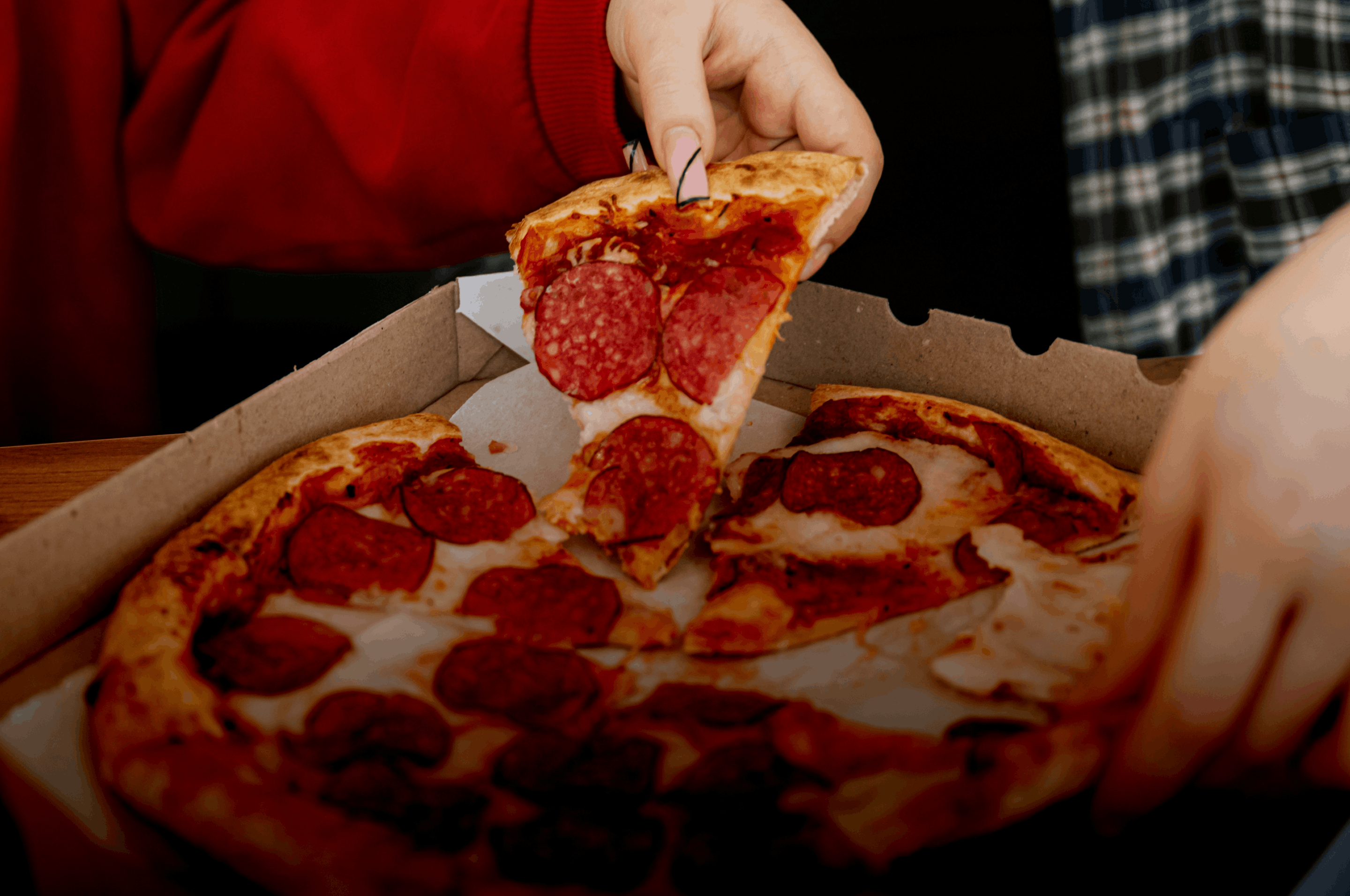 Hand lifting a pepperoni pizza slice from the box